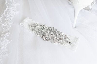 A garter is sitting on top of a white veil next to a pair of shoes. wedding. 