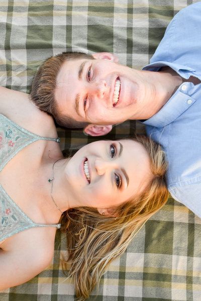 A man and a woman are laying on top of each other on a plaid blanket at White Point Beach