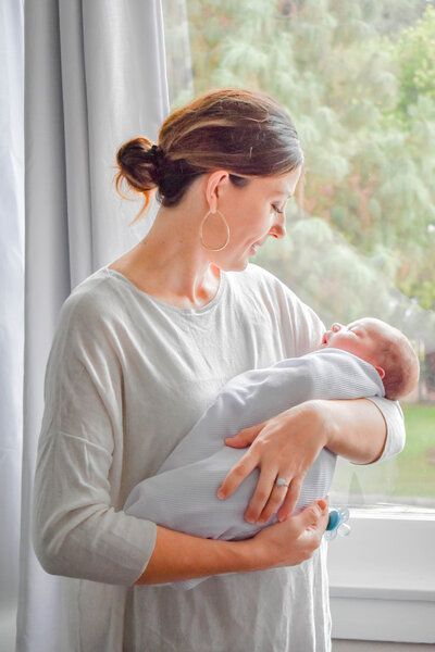 A woman is holding a baby in her arms in front of a window.