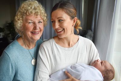 Two women are standing next to each other holding a baby. Generational family photo.