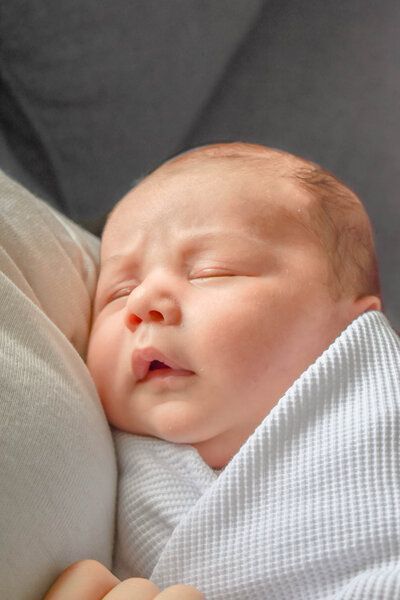 A newborn baby wrapped in a white blanket is sleeping on a pillow.