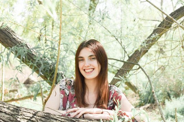 A woman is leaning on a tree branch and smiling at Ken Malloy Regional Park.