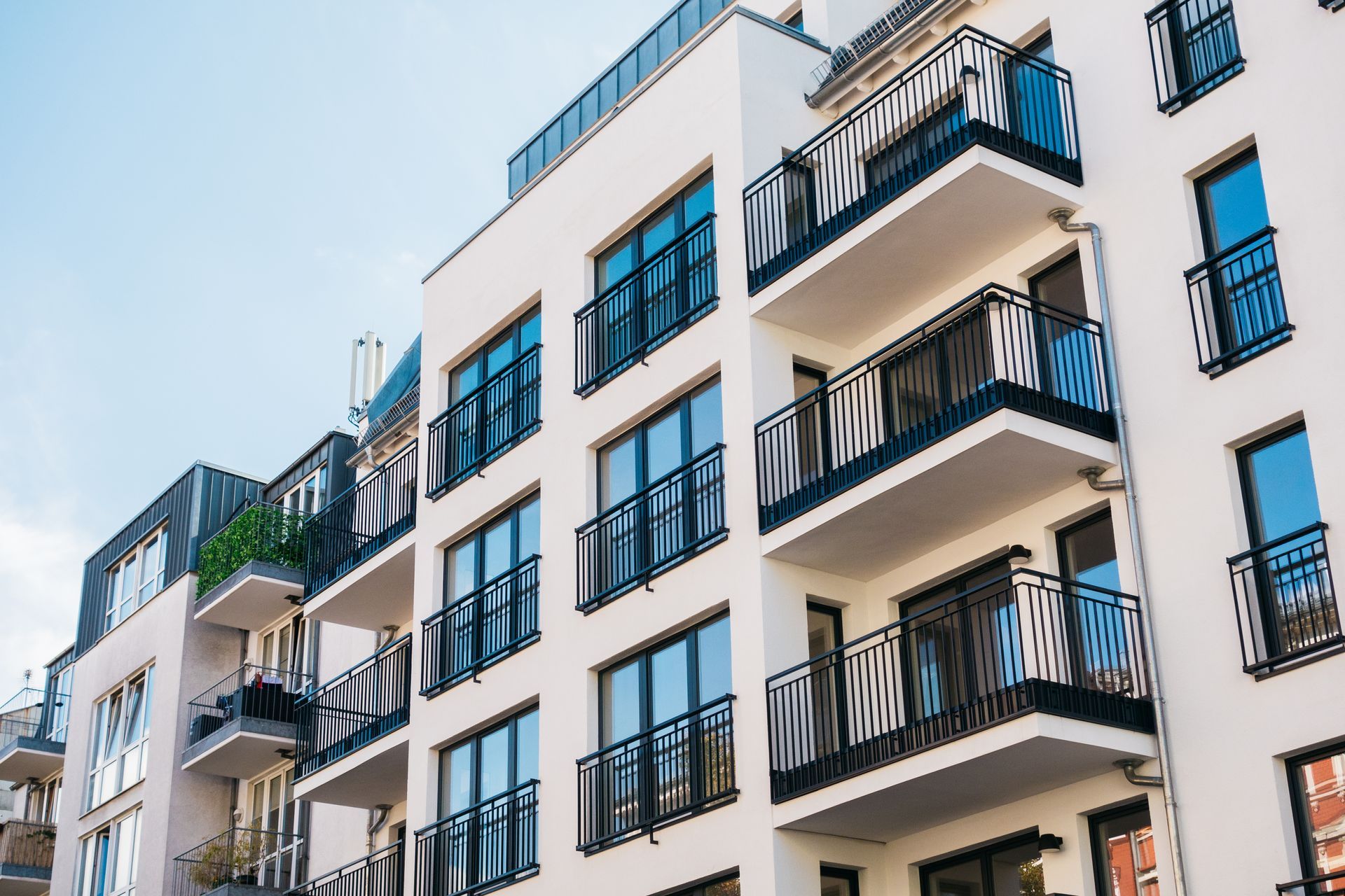Modern apartment building with white balconies and black railings under a blue sky