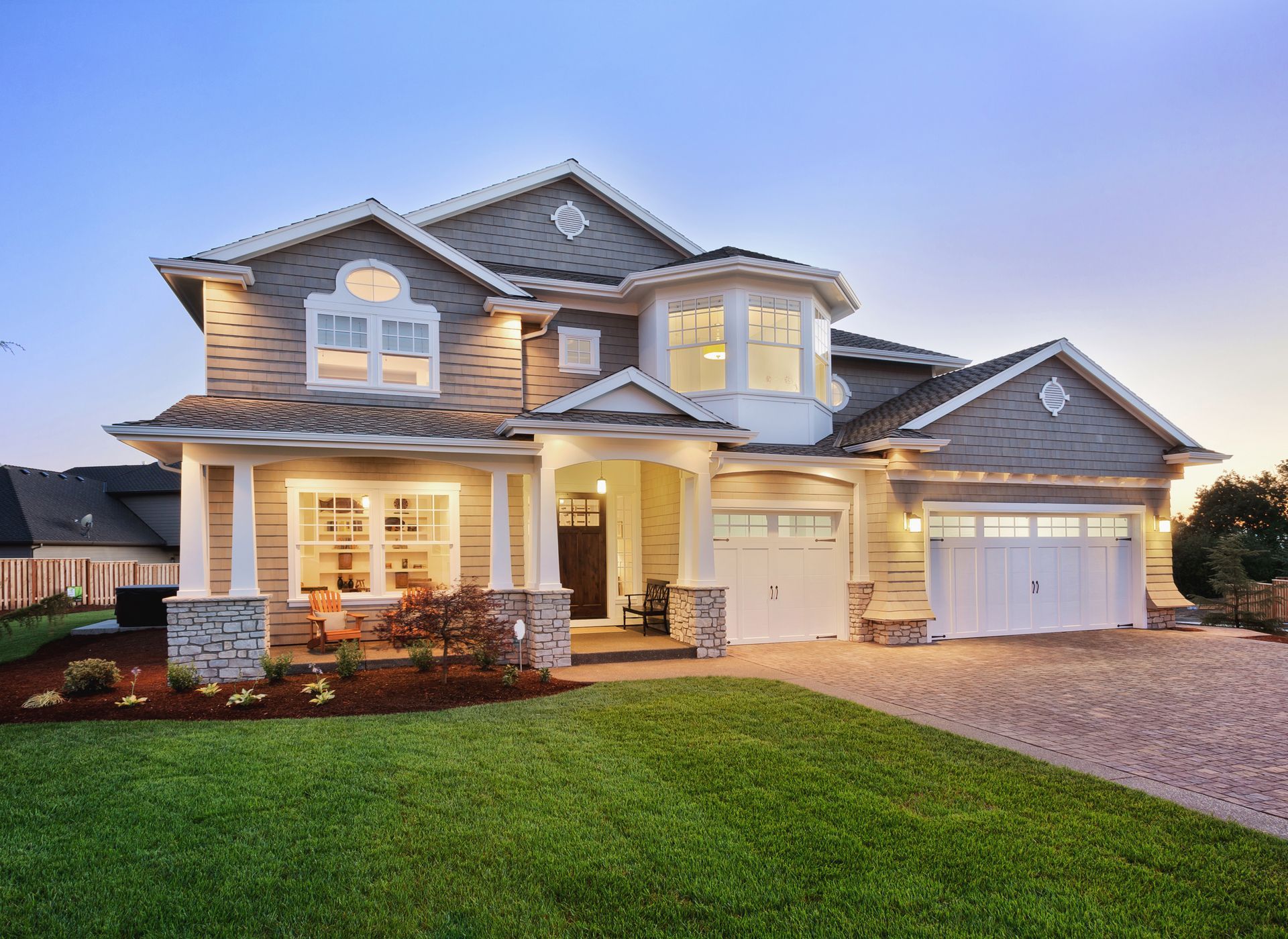 Two-story suburban house with lit windows and a front porch at dusk
