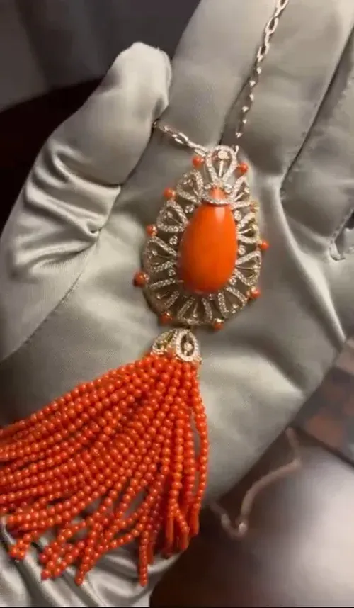 Orange beaded tassel pendant with silver filigree setting, held in a gloved hand Orange beaded tassel pendant with silver filigree setting, held in a gloved hand