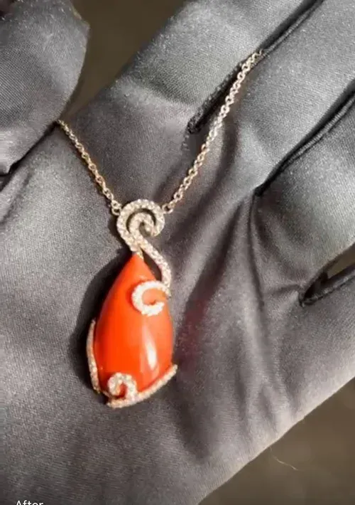 Orange teardrop pendant necklace with silver swirl accents on a black gloved hand Orange teardrop pendant necklace with silver swirl accents on a black gloved hand