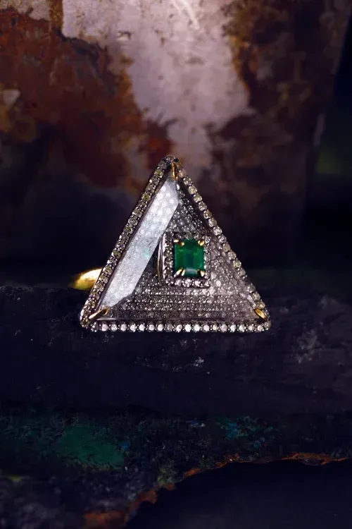 Triangular silver ring with a green gemstone on a dark textured surface