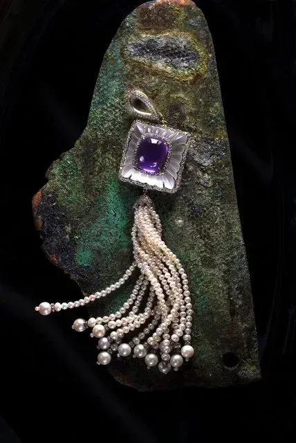 Dark green textured pendant with a purple square gem and dangling white bead strands on a black background Dark green textured pendant with a purple square gem and dangling white bead strands on a black background