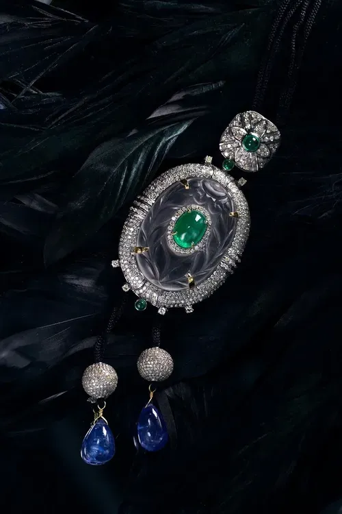 Silver brooch with green gem and blue teardrop dangles on a dark textured background
