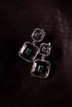 Four silver geometric earrings with green stones on dark leather background