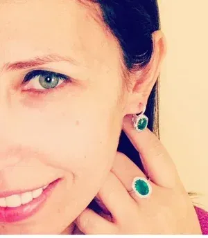 Close-up of a smiling woman wearing green gemstone earrings and a matching ring