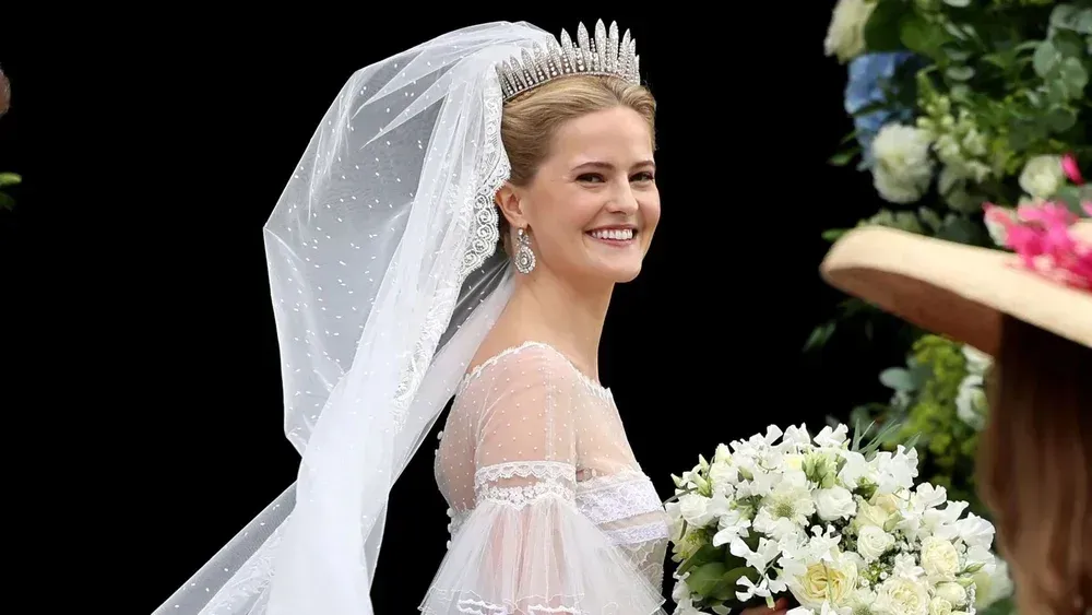 Bride in white gown and veil smiles while holding a bouquet outdoors at a wedding ceremony Bride in white gown and veil smiles while holding a bouquet outdoors at a wedding ceremony
