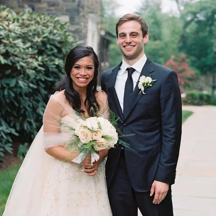 Bride and groom posing outdoors, smiling, with a white bouquet and navy suit Bride and groom posing outdoors, smiling, with a white bouquet and navy suit
