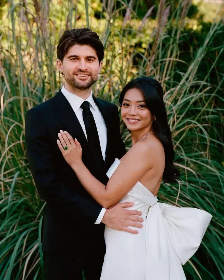 A couple in formal attire posing outdoors, with the woman in a white dress and the man in a black suit. A couple in formal attire posing outdoors, with the woman in a white dress and the man in a black suit.