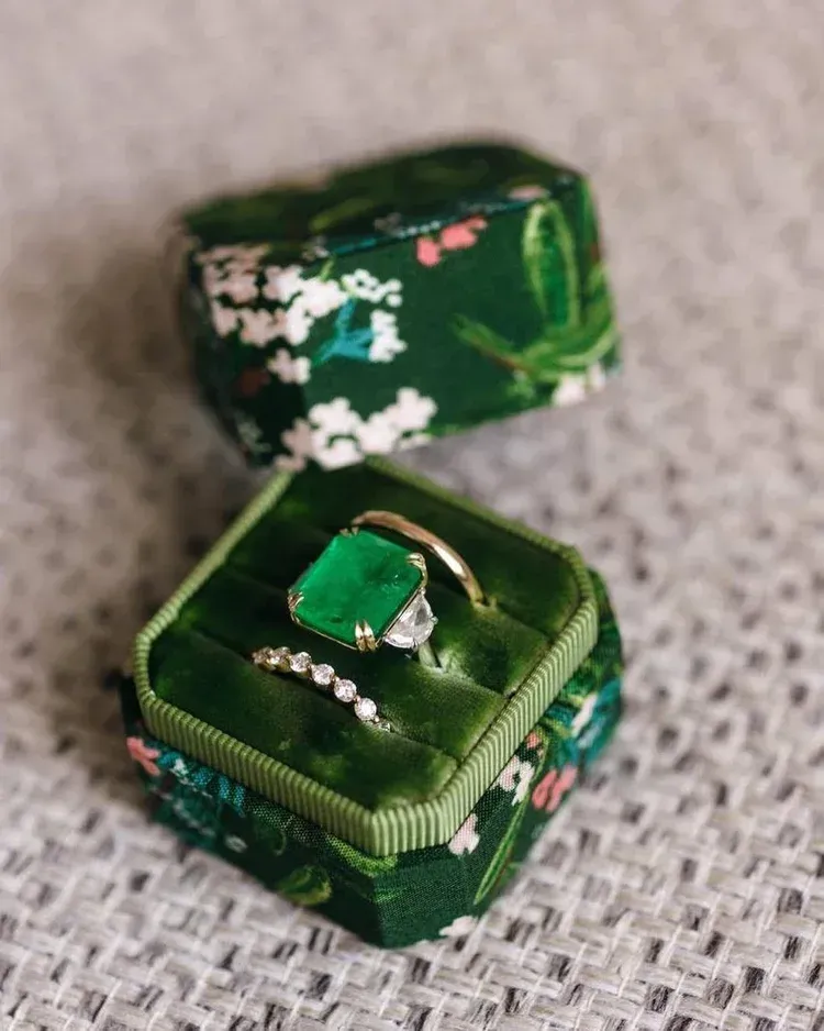 Two green ring boxes with floral accents, one open with a green gemstone ring Two green ring boxes with floral accents, one open with a green gemstone ring