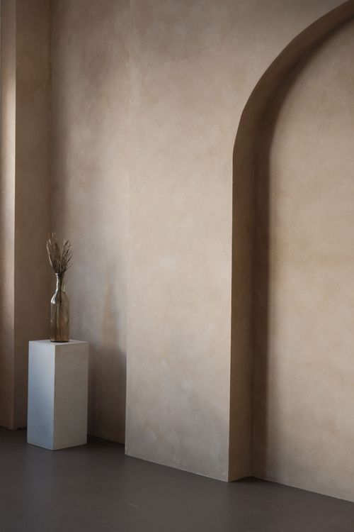 Minimalist interior with arched wall, pedestal, and small sculpture in warm neutral tones
