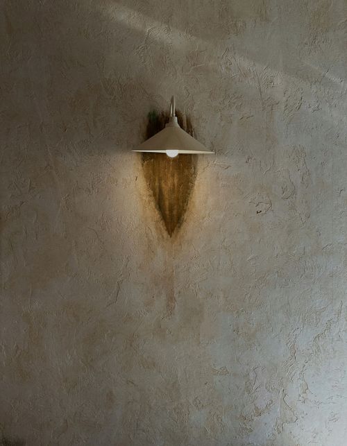 Wall-mounted light fixture casting a warm, downward glow on a textured beige wall.