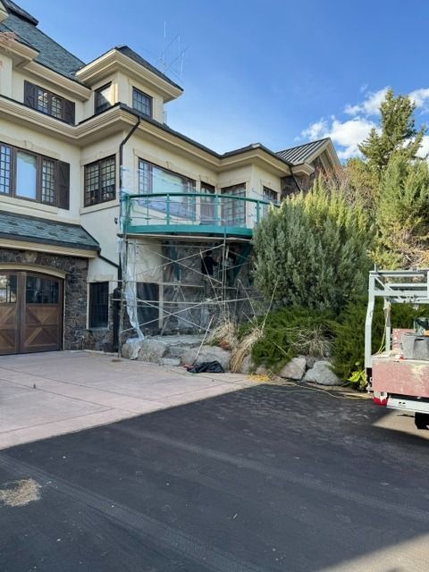 Luxury stone house exterior with teal balcony, driveway, and landscaping under a blue sky
