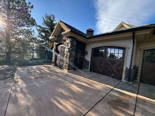 Sunny driveway beside a rustic house with stone columns and wooden garage doors