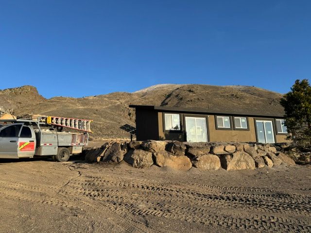 Desert roadside cabin with a parked utility truck and rocky hills under a clear blue sky