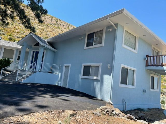 Blue house on a hillside with a white porch and balcony, beside a paved driveway.