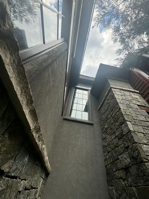 Looking up between stone walls at windows and a cloudy sky above