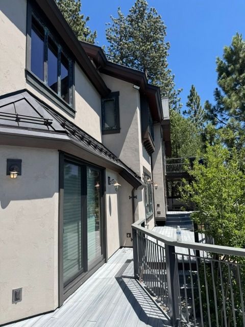 Balcony walkway beside a beige townhouse with glass railing and tall pine trees under a clear blue sky