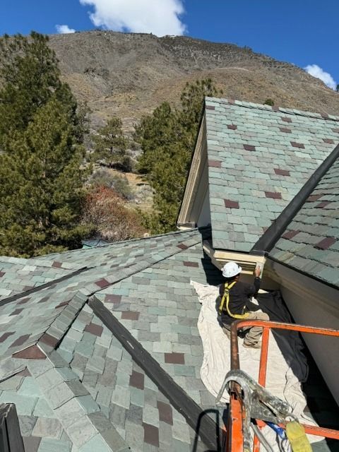 Rooftop with green-gray shingles, satellite dish, and mountain backdrop under blue sky