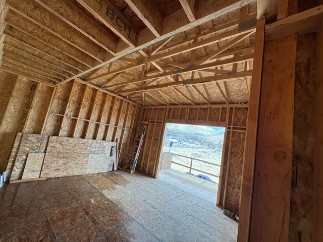 Unfinished wooden room interior with exposed rafters, plywood walls, and an open doorway overlooking mountains