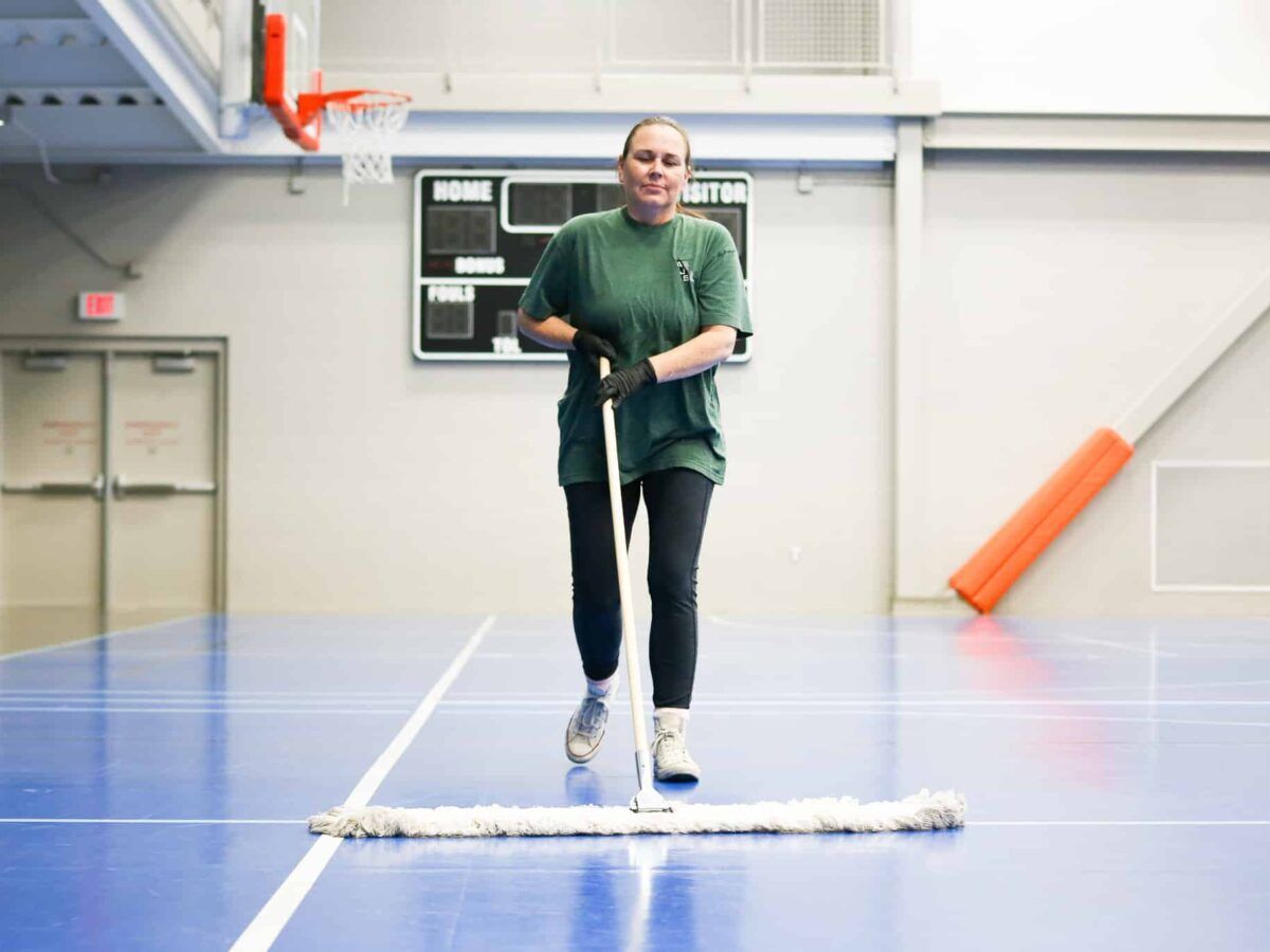 Person on skis indoors in a gym, standing on a white strip against a blue floor.