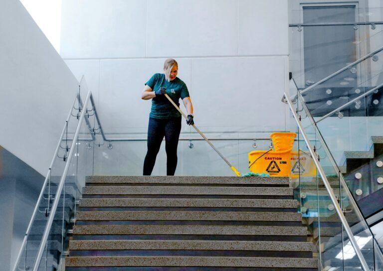 Worker mopping stairs in a building lobby beside a yellow wet floor sign