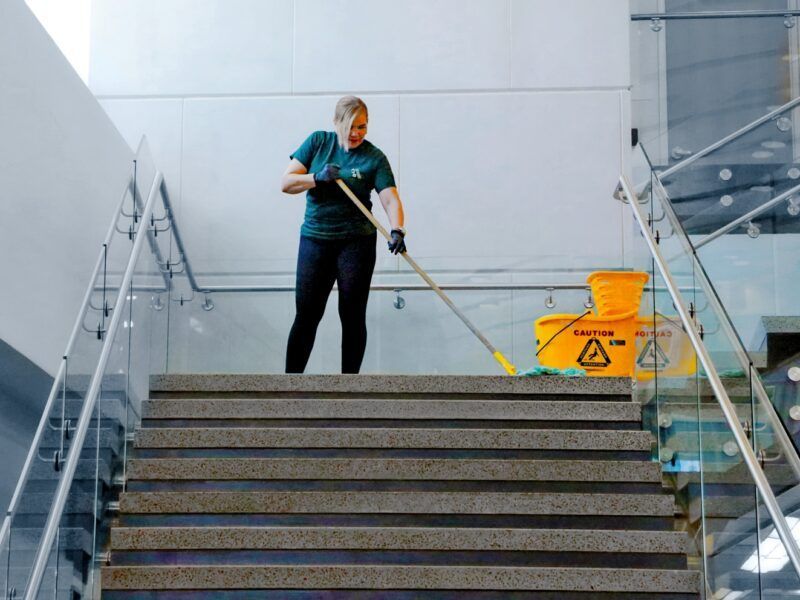 Worker mopping stairs beside a yellow wet floor sign in a modern building