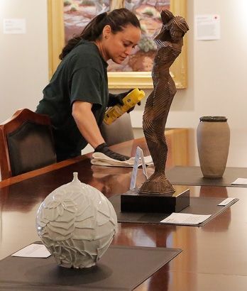 Person cleaning a sculpture in a gallery, with two artworks on a table nearby.