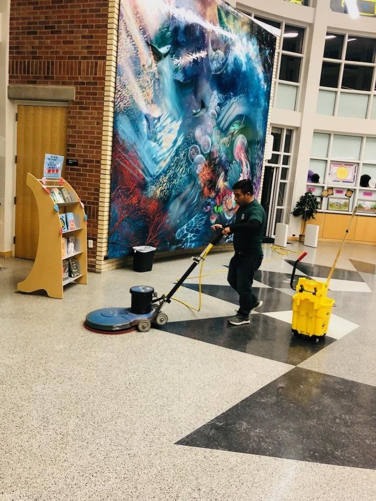 Person mopping a school hallway beside a large colorful mural, with cleaning supplies nearby