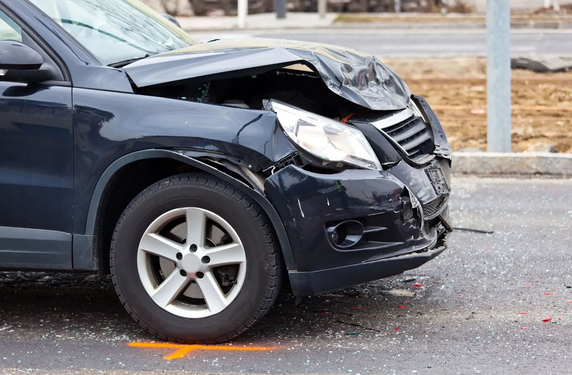 Dark blue SUV with front-end damage after a car accident, parked near a road.