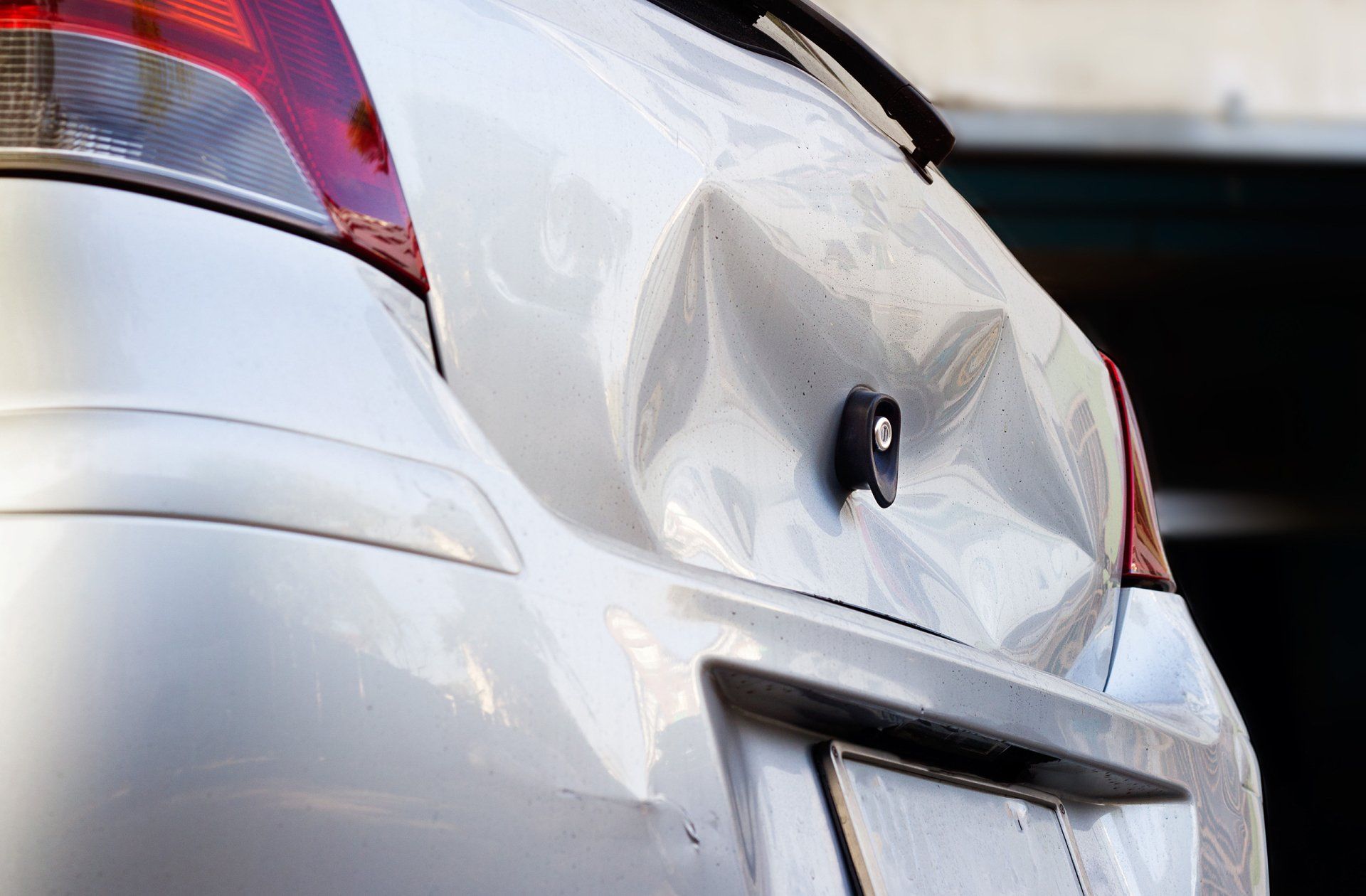 White car with a dented rear end, damaged from an accident.