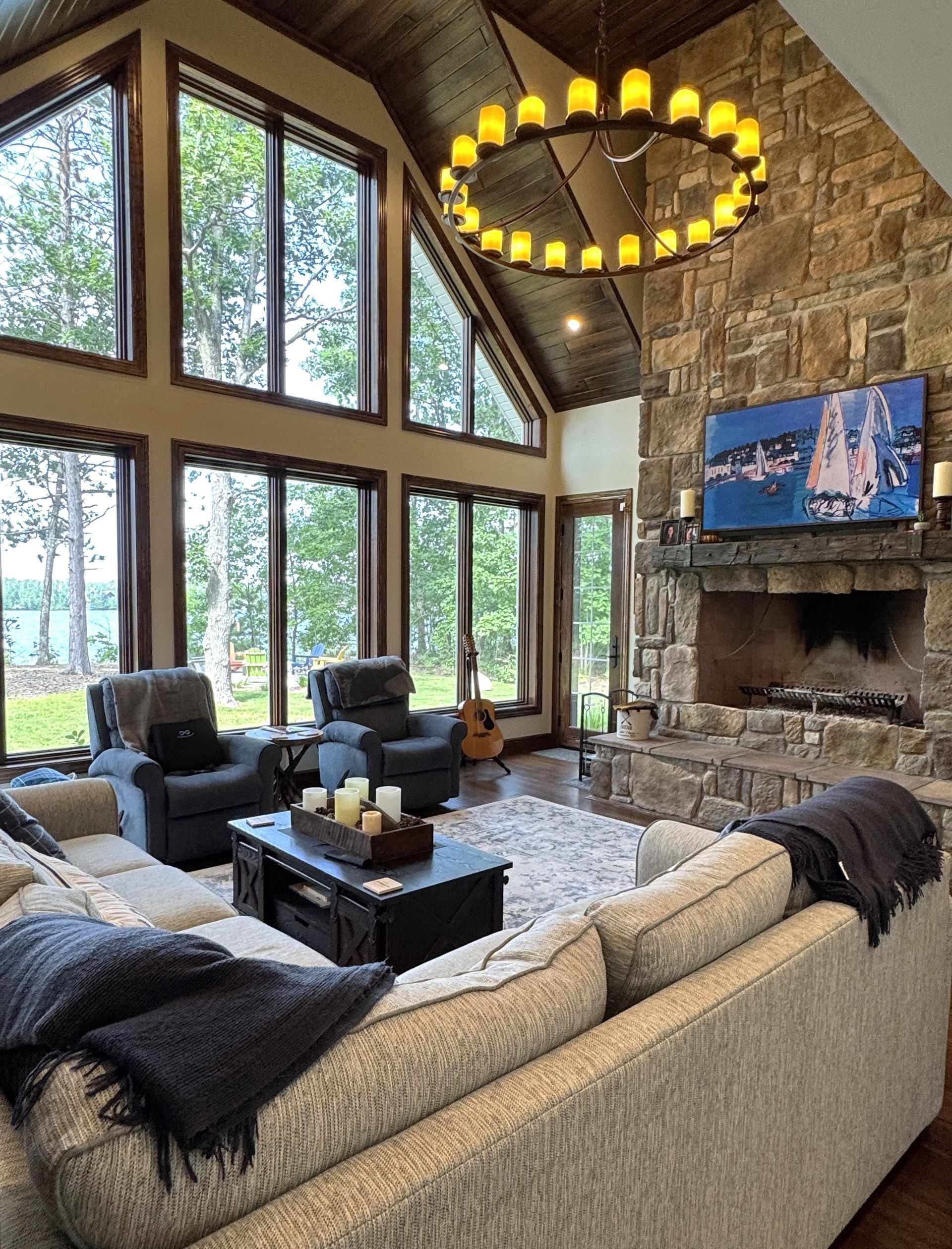Cozy stone great room with tall windows, large sectional sofa, chandelier, and fireplace with TV.