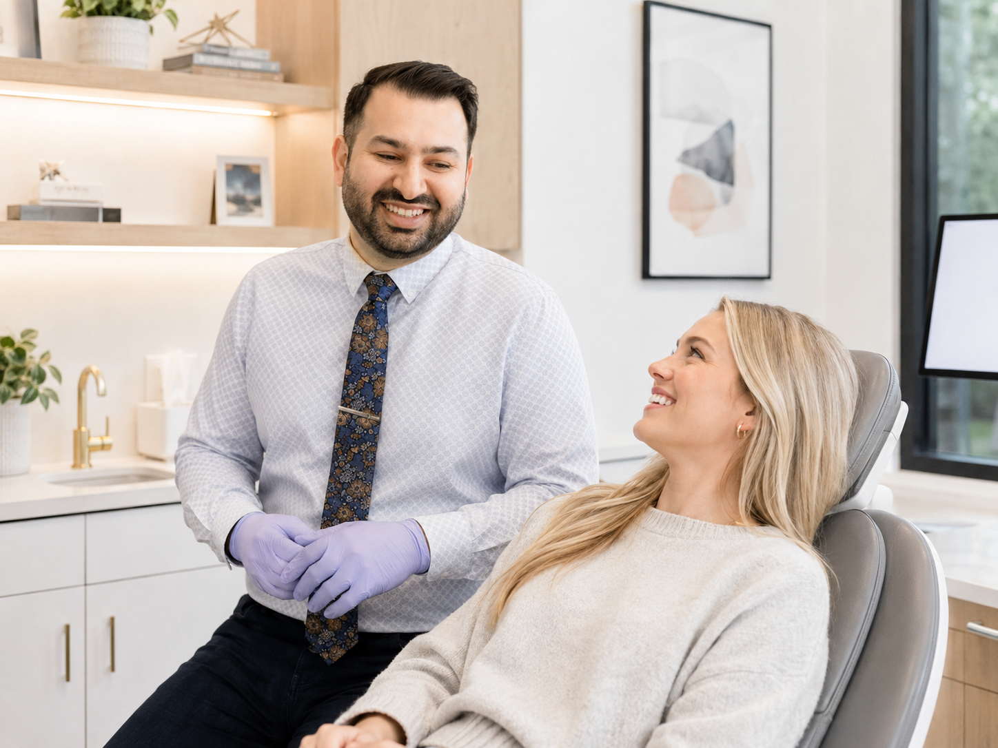 Dentist in purple gloves smiling beside a relaxed patient in a dental exam chair.