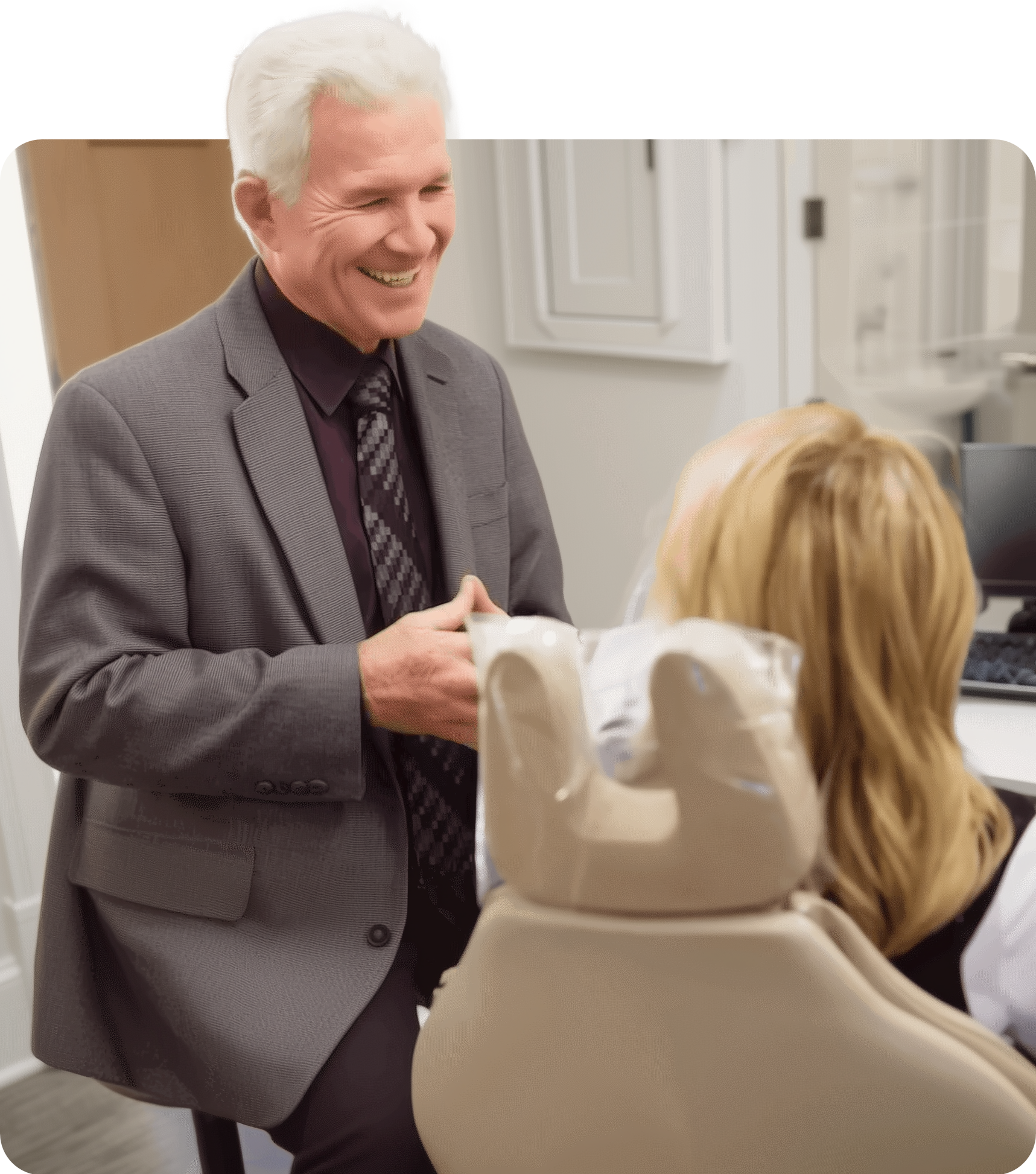 A professional in a grey blazer smiles while talking to a patient seated in a dental chair.