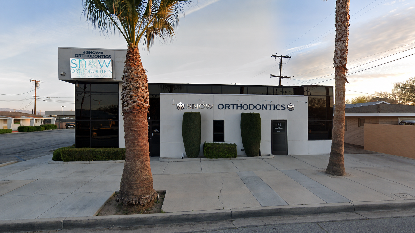 Exterior of a small business office with palm trees, sign reading “Bud Orthodontics” at sunset