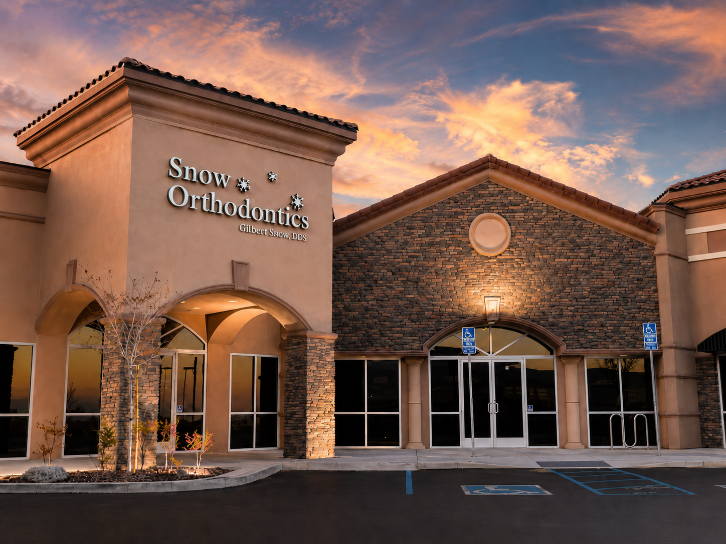 Stone-front Orthodontics office at sunset with lit windows and a fountain in front
