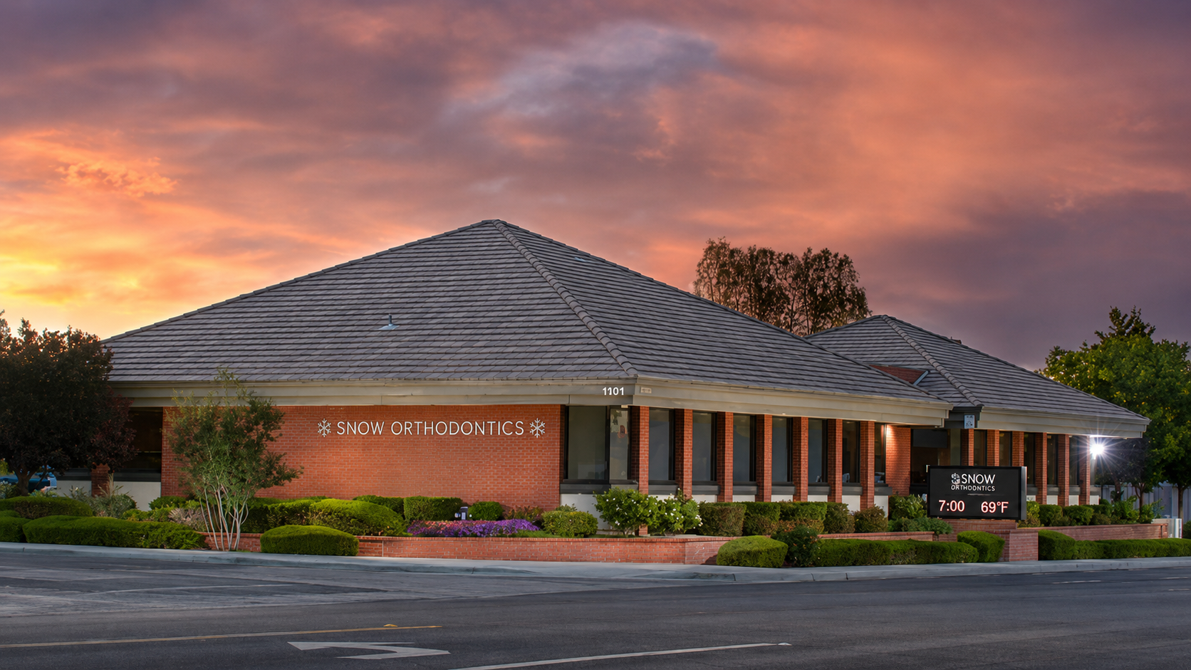 Brick commercial building at sunset with a peaked roof, columns, and pink-orange clouds in the sky
