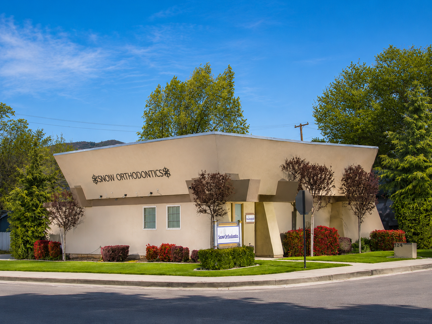 Modern curved white building with landscaping and trees under a blue sky