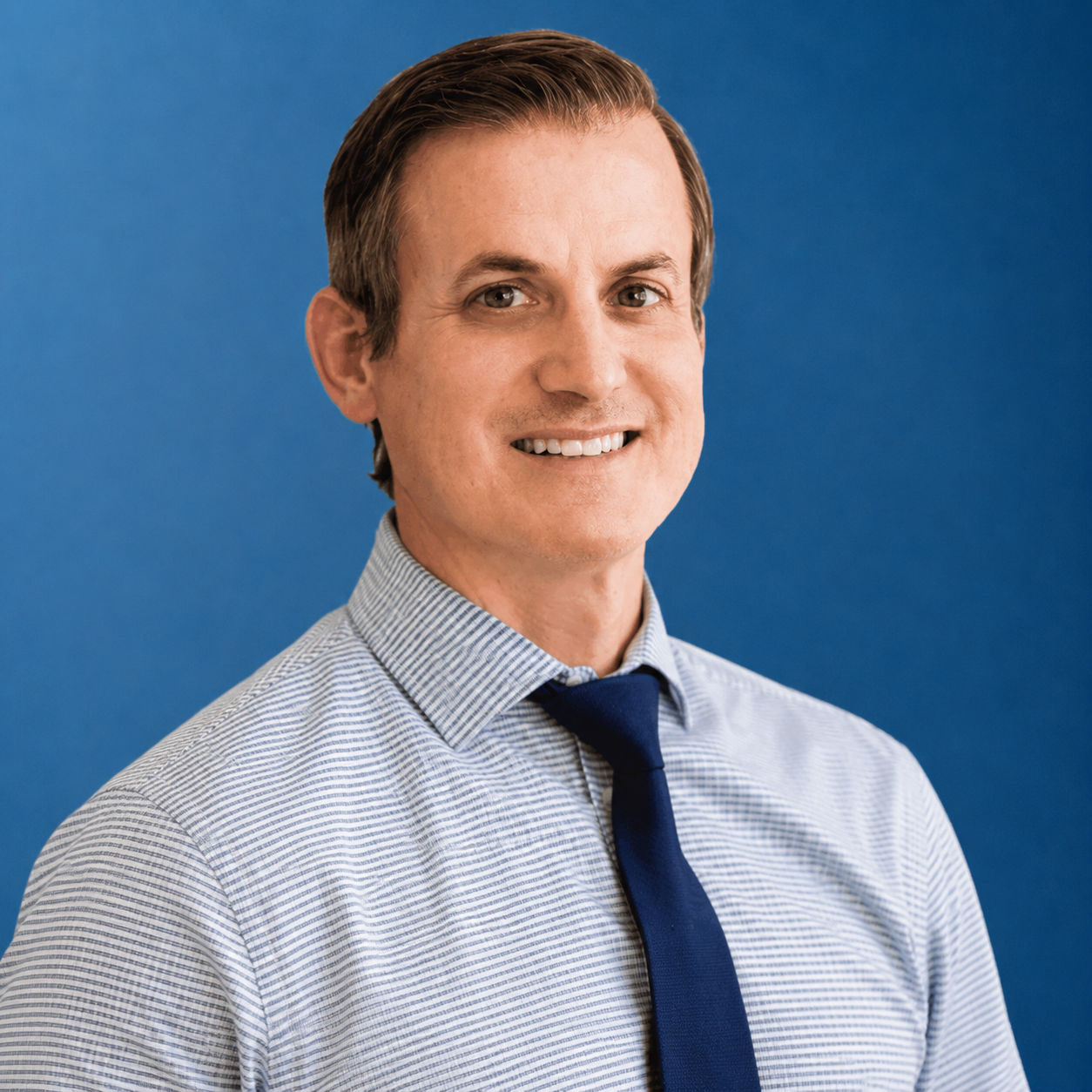 Smiling person in a light blue striped shirt and navy tie against a blue background