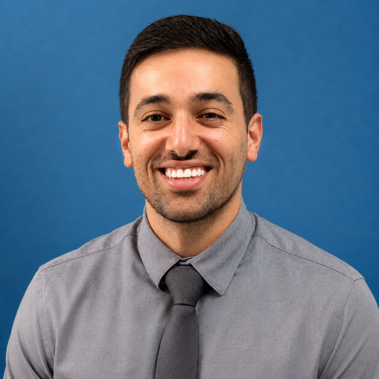Smiling man in a gray shirt and tie against a blue background