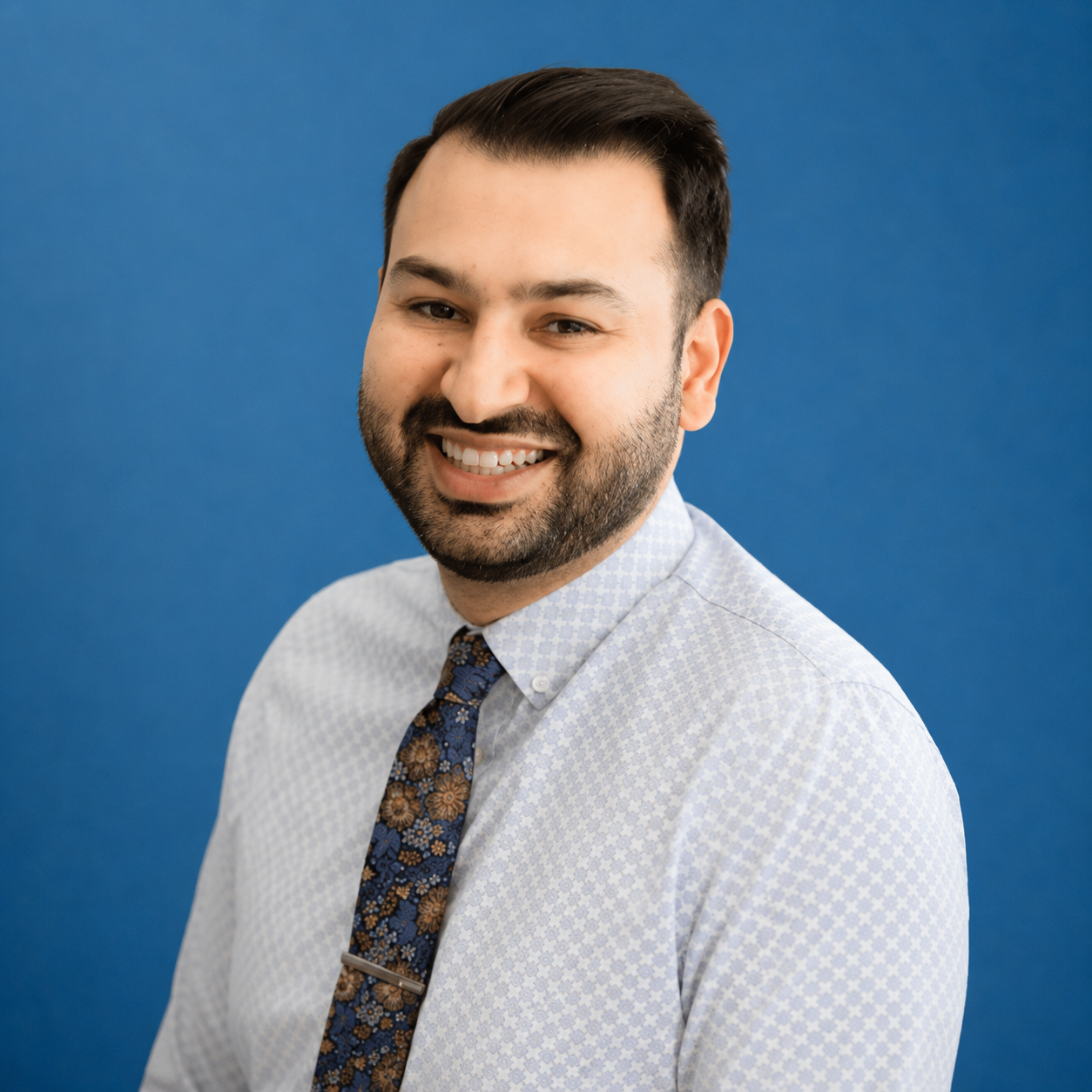 Smiling man in a light shirt and patterned tie against a blue background