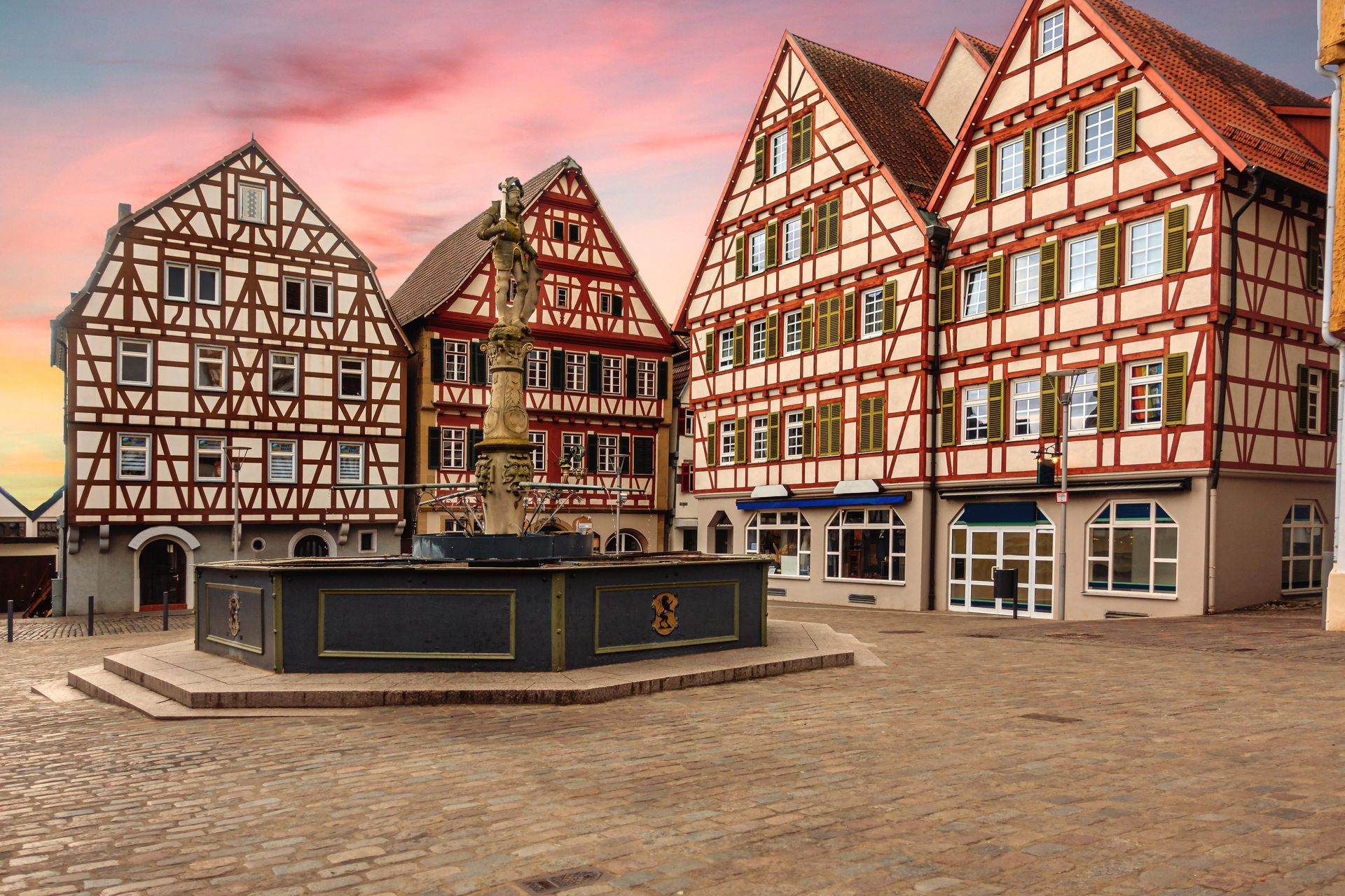 Bâtiments historiques à colombages autour d'une fontaine de place de marché au coucher du soleil