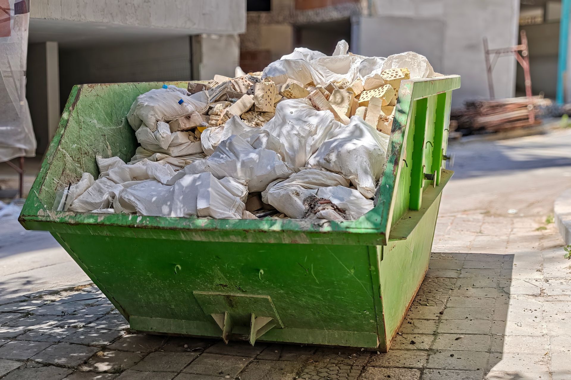 A bright green dumpster filled with white Styrofoam scraps sits on a paved surface near a building.