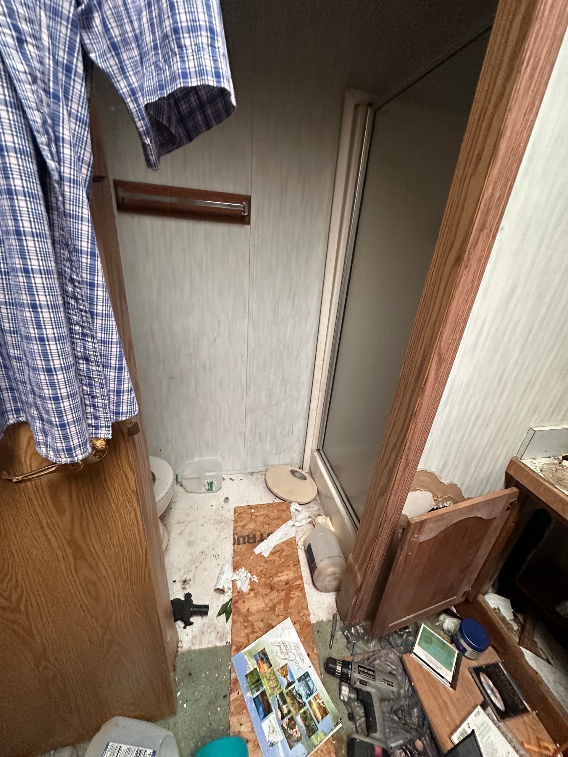 A cluttered, dimly lit bathroom interior with a shower stall, wood-paneled walls, and debris scattered on the floor.