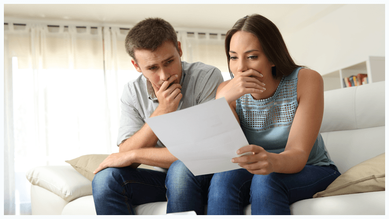 A man and a woman are sitting on a couch looking at a piece of paper.